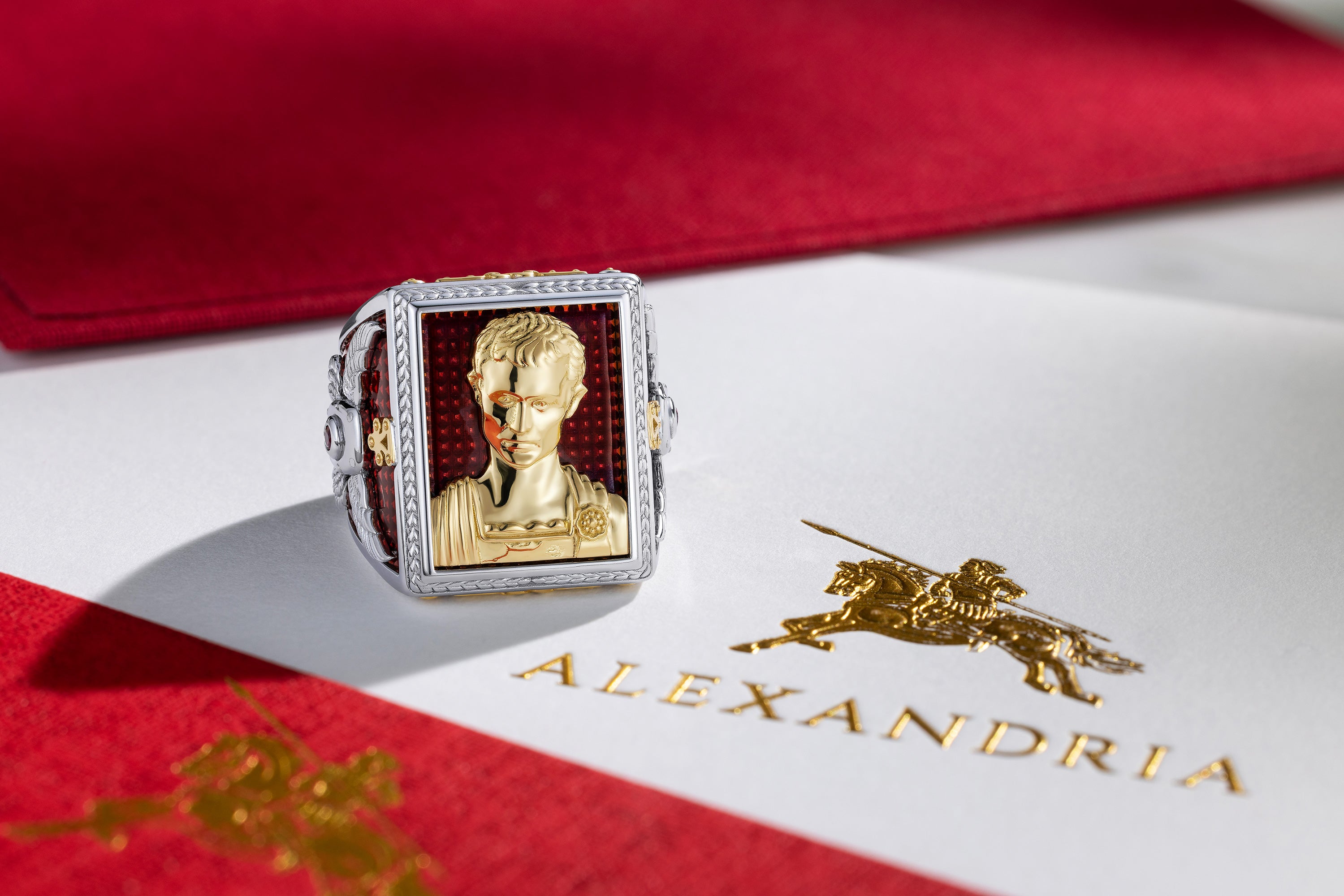 Gold ring with a portrait on a red and white box labeled 'Alexandria'.