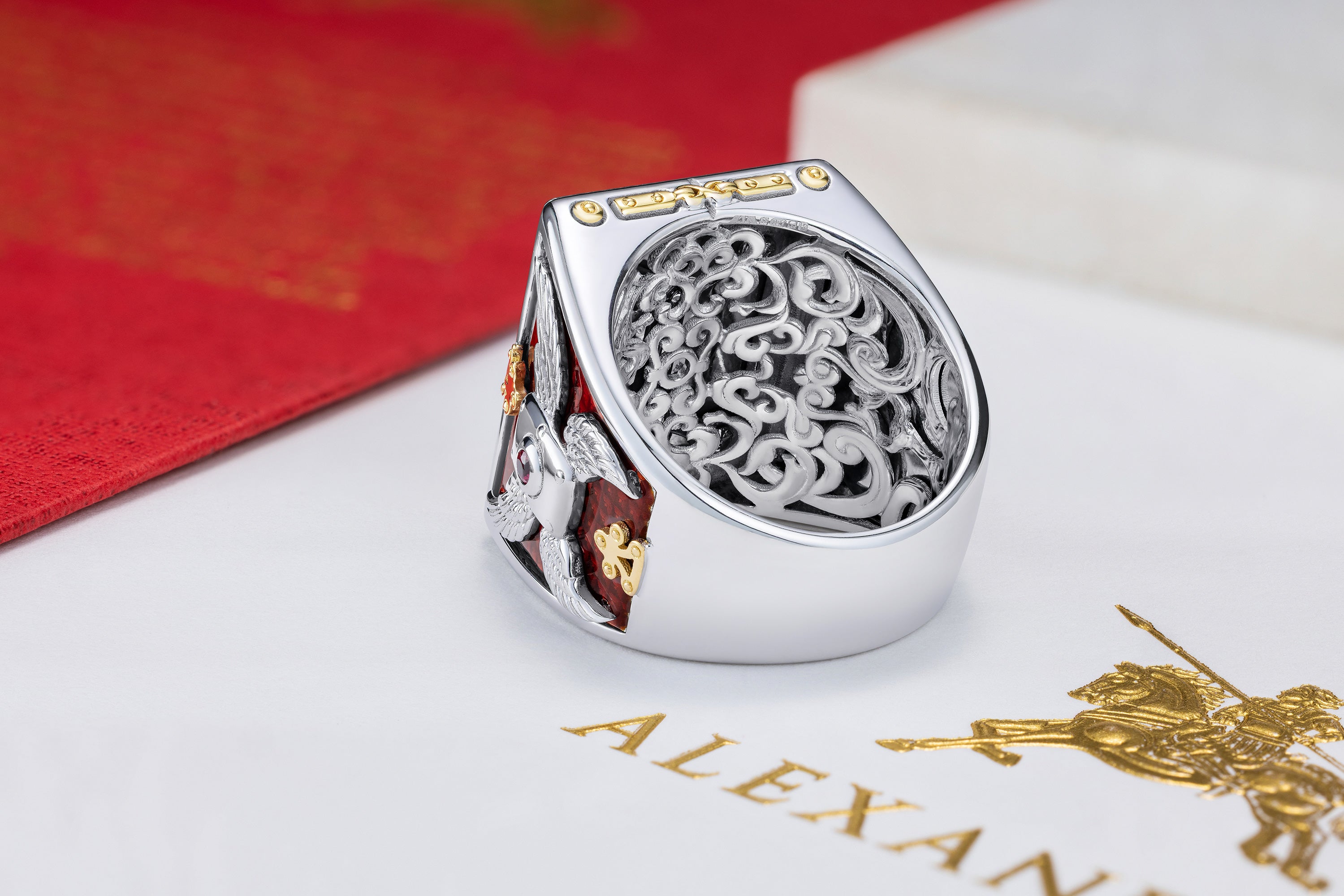 White gold ring with intricate design roman motif pattern on a red and white background